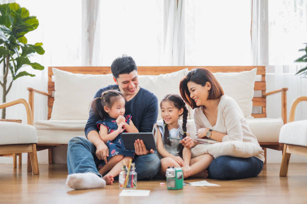 Happy Asian family using tablet, laptop for playing game watching movies, relaxing at home for lifestyle concept